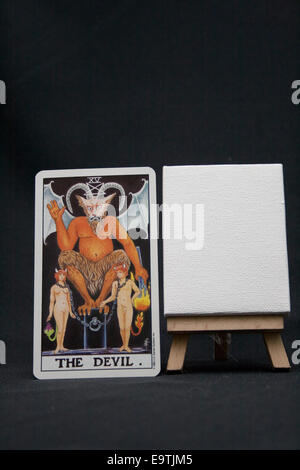 Der Teufel-Tarot-Karte neben einer leeren Leinwand auf einem dunklen Hintergrund. Stockfoto