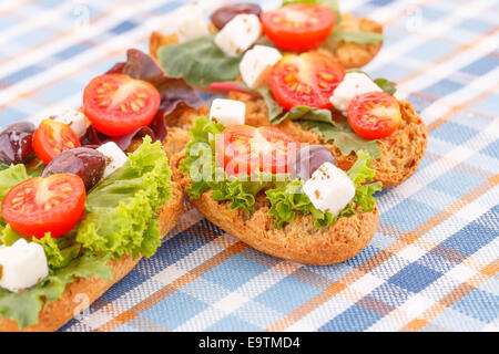 Sandwiches mit Zwieback, Gemüse, Oliven und Feta-Käse auf bunte Tischdecke. Stockfoto