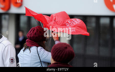 Eine Frau kämpft mit ihrem roten 'Keep Calm and Carry On' Schirm an Brighton Strandpromenade bei stürmischem Wetter Stockfoto