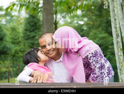 Glückliche südostasiatischen muslimischen Familie, küssen auf Vaters Gesicht, outdoor-Lifestyle im grünen Naturpark. Stockfoto