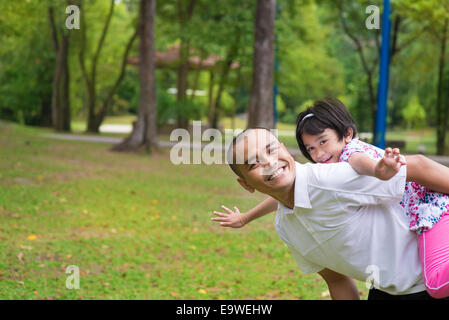 Vater und Tochter spielen im Outdoor-Garten Park Huckepack. Glücklich südostasiatischen Familie leben Lebensstil. Stockfoto