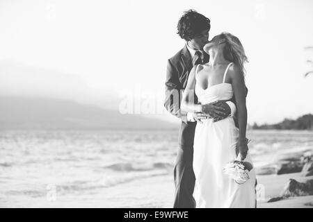 Schöne Hochzeitspaar, Braut und Bräutigam küssen am Strand bei Sonnenuntergang. Schwarz / weiß Foto Stockfoto