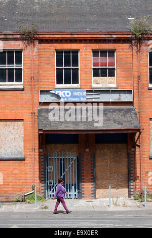 Frau in lila geht vorbei an stillgelegten aus rotem Backstein gewerblichen Räumlichkeiten Stockfoto