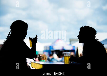 Zwei junge Frau Mädchen Silhouette sitzen reden trinken Pints Lager-Bier-Apfelwein an das National Eisteddfod of Wales 2014 Stockfoto