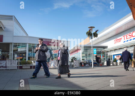 Mit einer großen Jacke Woman applying und telefonieren mit ihrem Handy geht mit einem Mann durch ein modernes Einkaufszentrum. Stockfoto