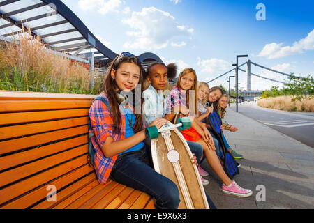 Positive Mädchen mit Skateboards sitzen auf lange Bank Stockfoto