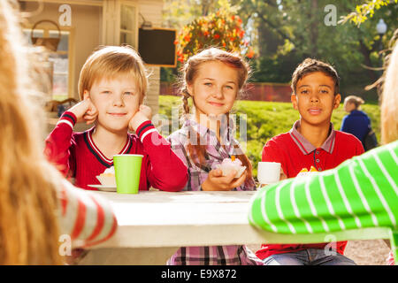 Glückliche Kinder trinken Tee mit Cupcakes sitzen Stockfoto