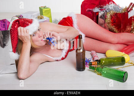 Weibliche Partei-Goer auf dem Boden trägt ein Kostüm Santa Outfit und Alkohol zu trinken Stockfoto