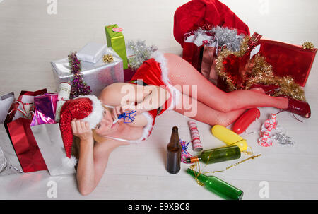 Weibliche Partei-Goer auf dem Boden trägt ein Kostüm Santa Outfit und Alkohol zu trinken Stockfoto