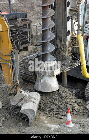 Nahaufnahme eines kontinuierlichen Flug Auger Stapeln Rig bei der Arbeit auf einem Fundament mit Bagger Schaufel clearing verwöhnen Kegel Marken 1 abgeschlossen Stockfoto