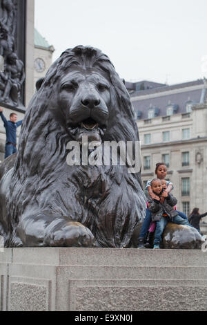 Trafalgar Square. London. England.  Ein "Landseer Löwe" auf Sockel im Vordergrund mit Afro-Karibischen Kinder posieren für Eltern Stockfoto