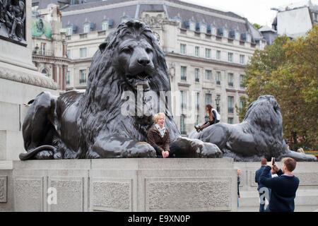 Trafalgar Square. London. England.  Ein "Landseer Löwe" auf Sockel im Vordergrund mit junge Frau posiert für Menschen zu fotografieren. Stockfoto