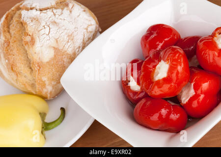 Kirsch-Paprika gefüllt mit cremigen Käse in Olivenöl in einer weißen Schüssel serviert. Gelbe Paprika und Brot auf einem weißen Teller. Stockfoto