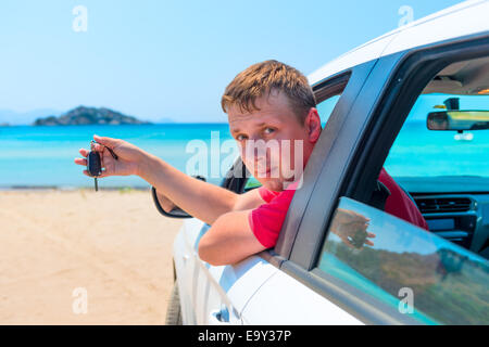 der Mann mit dem Schlüssel für das Auto schaut aus dem Fenster auf dem Hintergrund des Meeres Stockfoto