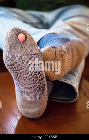 Füßen aufgestützt auf einen Couchtisch mit abgenutzten Socken ein Loch mit einer Zehe aus ihnen kleben. Stockfoto