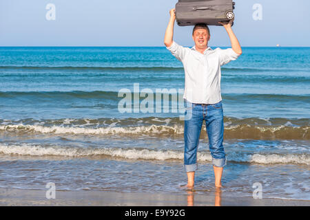 glücklicher Mann mit Koffer barfuß im Meer Stockfoto