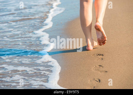 wohlgeformte weibliche Beine hinterlassen Spuren auf einem sandigen Strand Stockfoto