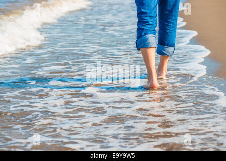 männliche Beine in Jeans zu Fuß entlang der sandigen Küste Stockfoto