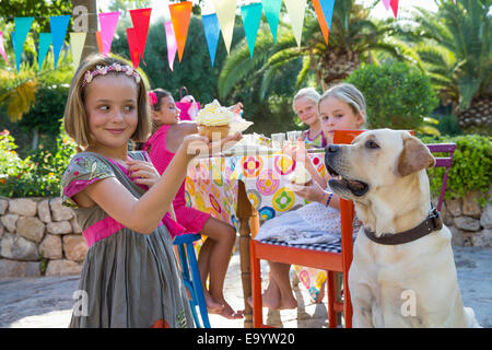 Mädchen an der Geburtstagsfeier mit Hund hält cupcake Stockfoto