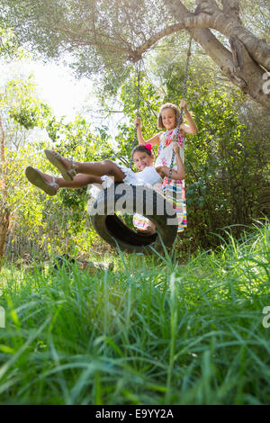 Zwei Mädchen sitzen und stehen auf Baum-Schaukel im Garten Stockfoto