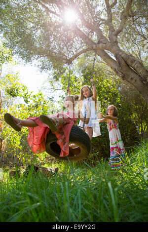 Niedrigen Winkel Ansicht von drei Mädchen spielen auf Baum Reifenschaukel im Garten Stockfoto