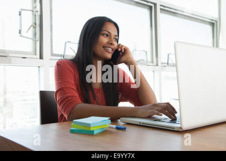 Frau auf Smartphone mit Laptop zu Hause Stockfoto