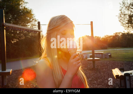 Junge Frau essen Eiscreme-Kegel im Park bei Sonnenuntergang Stockfoto