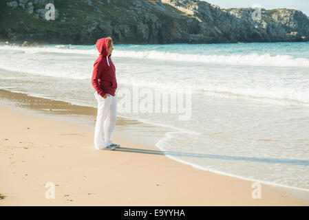 Reife Frau am Strand mit Händen in den Taschen, Camaret-Sur-Mer, Bretagne, Frankreich Stockfoto