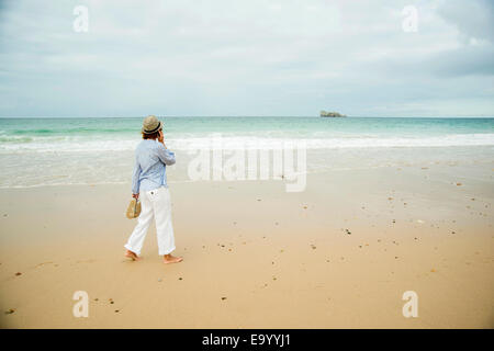 Reife Frau spazieren am Strand im Chat auf Smartphone, Camaret-Sur-Mer, Bretagne, Frankreich Stockfoto