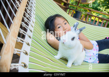 Junge Asiatin auf Hängematte mit Hauskaninchen Stockfoto