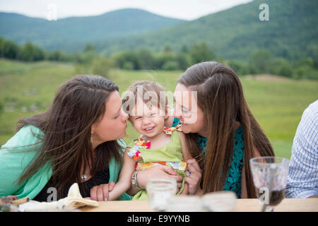 Babymädchen sitzen zwischen zwei jungen Frauen Stockfoto