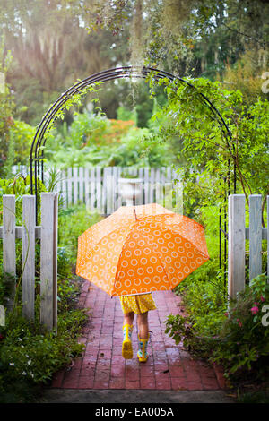 Mädchen zu Fuß durch Gartentor mit Regenschirm Stockfoto