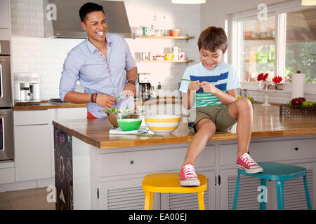 Vater und Sohn in Küche, junge sitzt an Theke Stockfoto