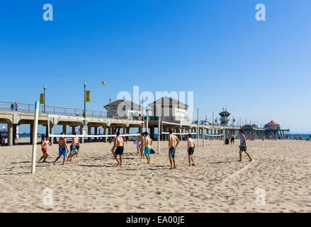 Junge Männer spielen Beachvolleyball vor dem Pier in der Innenstadt von Huntington Beach, Orange County, Kalifornien, USA Stockfoto