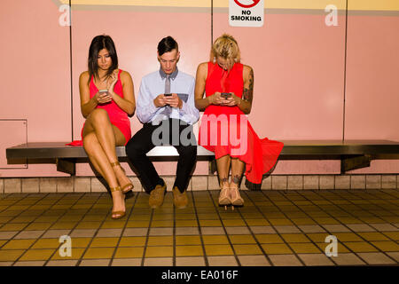 Drei junge Erwachsene Freunde SMS auf Smartphones in u-Bahnstation sitzend Stockfoto
