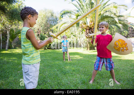 Drei Kinder im Garten spielen mit Spielzeug Schwerter Stockfoto