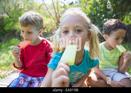 Porträt von drei Kindern im Garten essen Eis am Stiehl Stockfoto