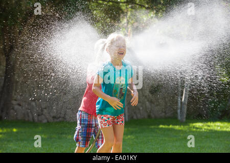 Junge Mädchen im Garten zu jagen, mit Wasser sprinkler Stockfoto