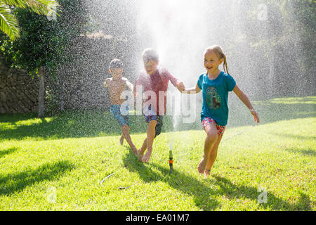 Drei Kinder im Garten fließt Wasser sprinkler Stockfoto