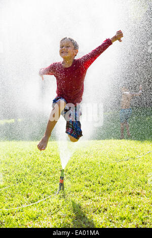 Junge, springen über Wasser Sprinkler im Garten Stockfoto