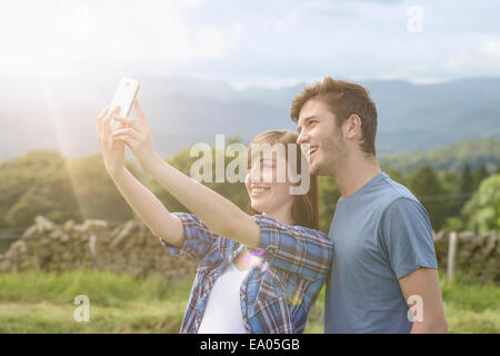 Junges Paar unter Selbstportrait auf Handy in Landschaft unter sonnigem Himmel Stockfoto