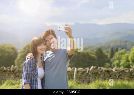 Junges Paar unter Selbstportrait auf Handy in Landschaft unter sonnigem Himmel Stockfoto