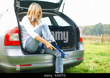 Frau sitzt am Heck des Autos Socken anziehen Stockfoto