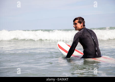 Junger Mann sitzt auf Surfbrett im Meer Stockfoto