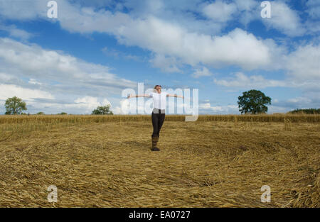 Reife Bäuerin feiert mit Armen in abgeernteten Weizenfeld öffnen Stockfoto