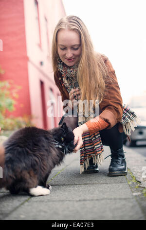 Junge Frau Petting schwarze Katze auf Bürgersteig Stockfoto