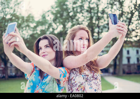 Zwei junge Freundinnen nehmen Selfie auf Smartphones nebeneinander Stockfoto