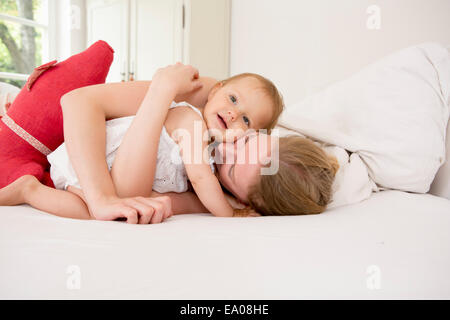 Mutter umarmt Baby-Tochter auf Bett Stockfoto