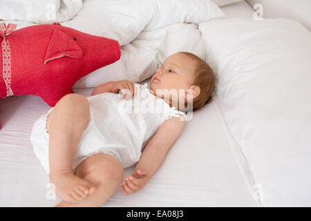 Babymädchen auf Bett, Blick auf Stofftier liegend Stockfoto