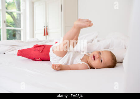 Babymädchen auf dem Bett liegend mit Beine angehoben Stockfoto